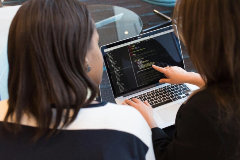 2 women talking about code on laptop monitor